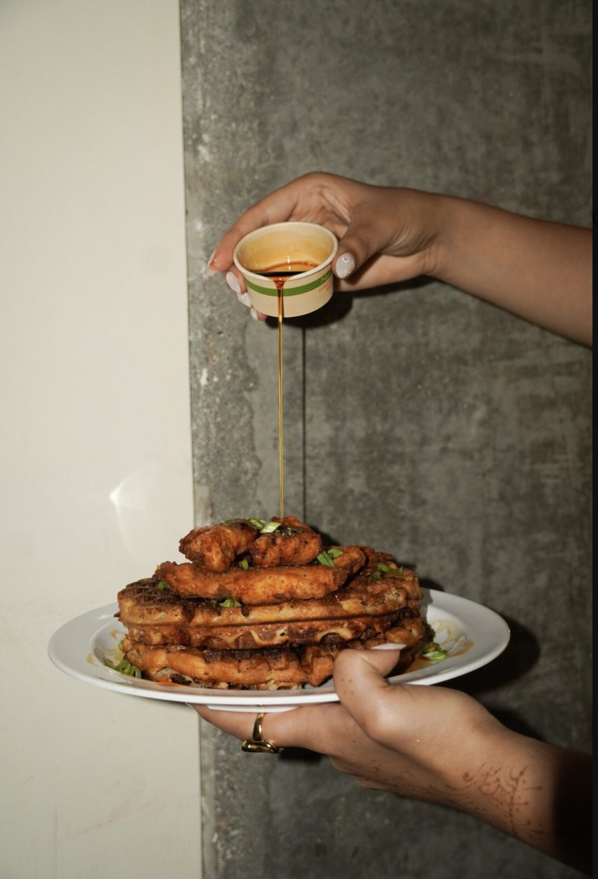 Syrup poured over a stack of chicken and waffles at Shattuck & Butter