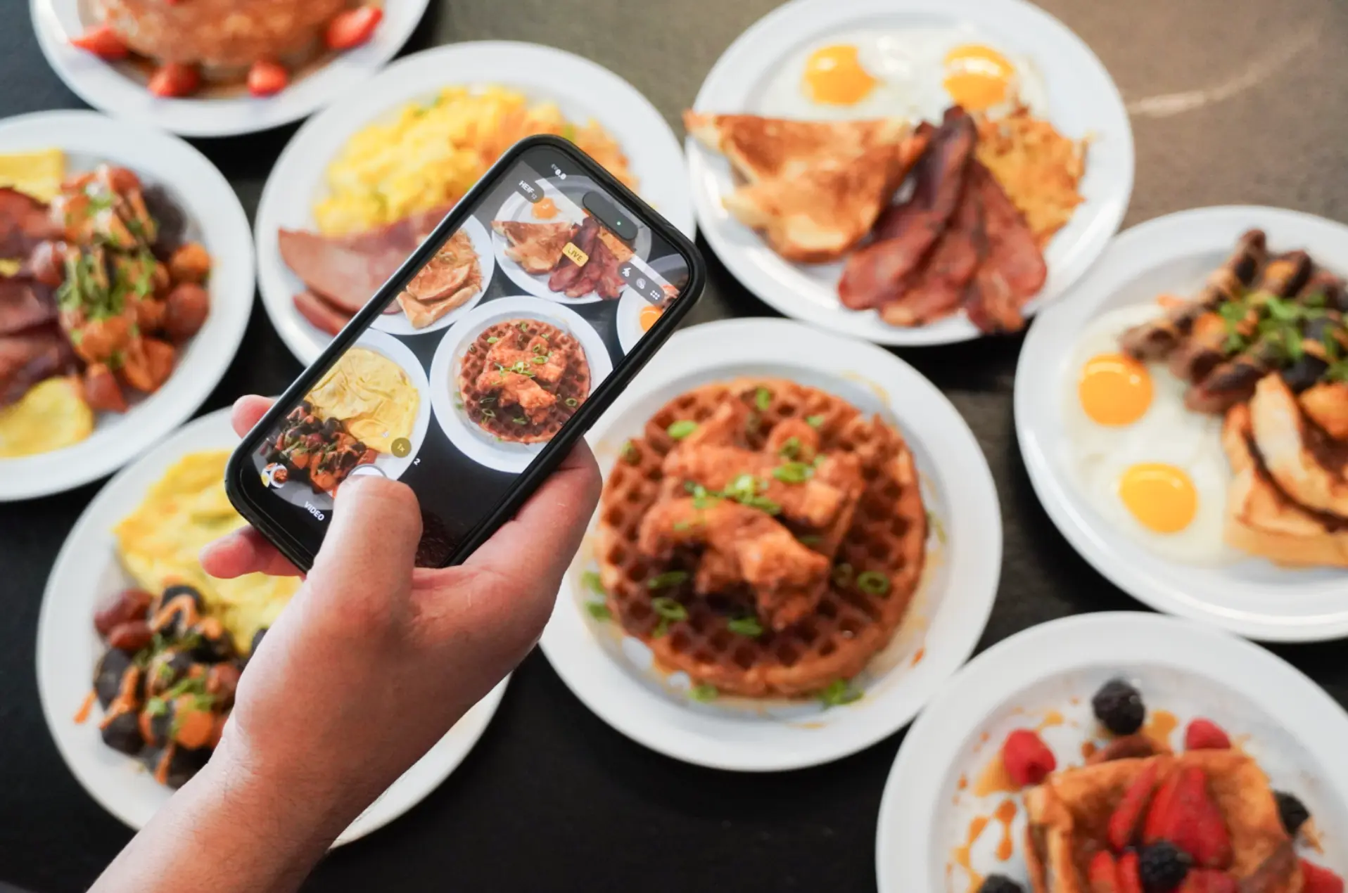 A table full of brunch plates being photographed on a phone